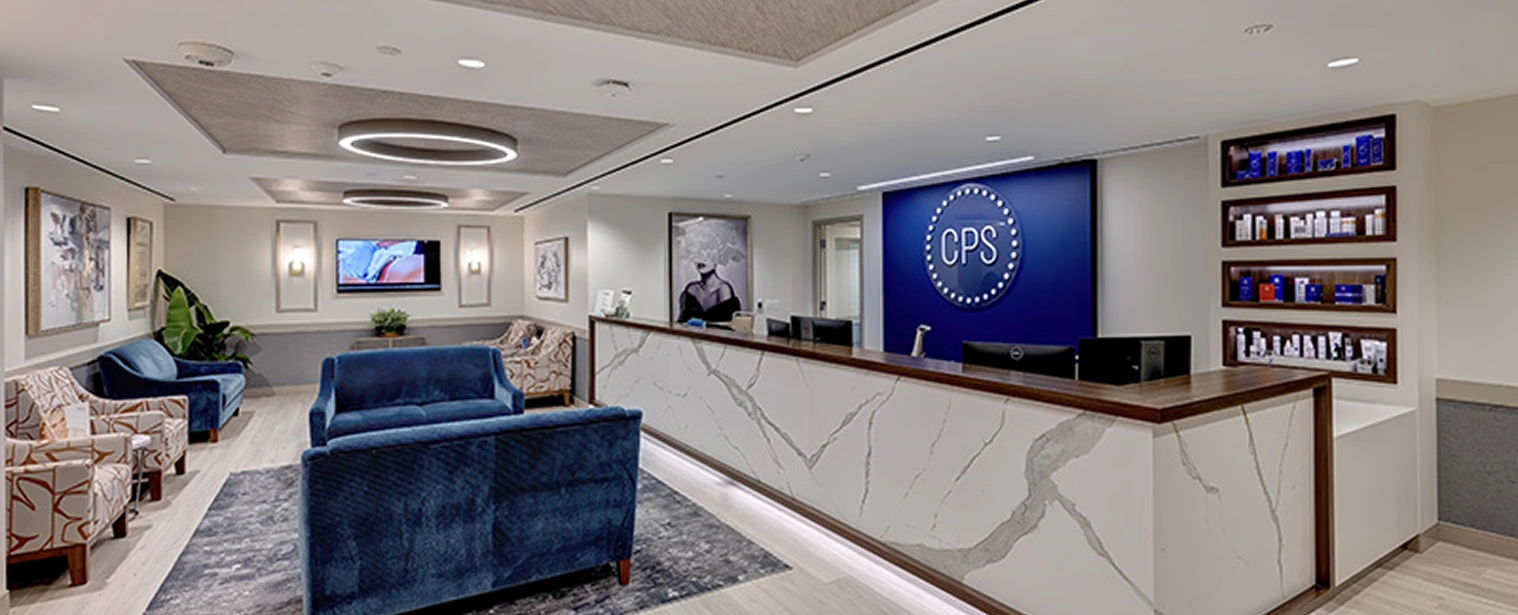 CPS main office reception with blue velvet sofa, marble counter, CPS logo display, artwork, shelving with products, and modern architectural ceiling